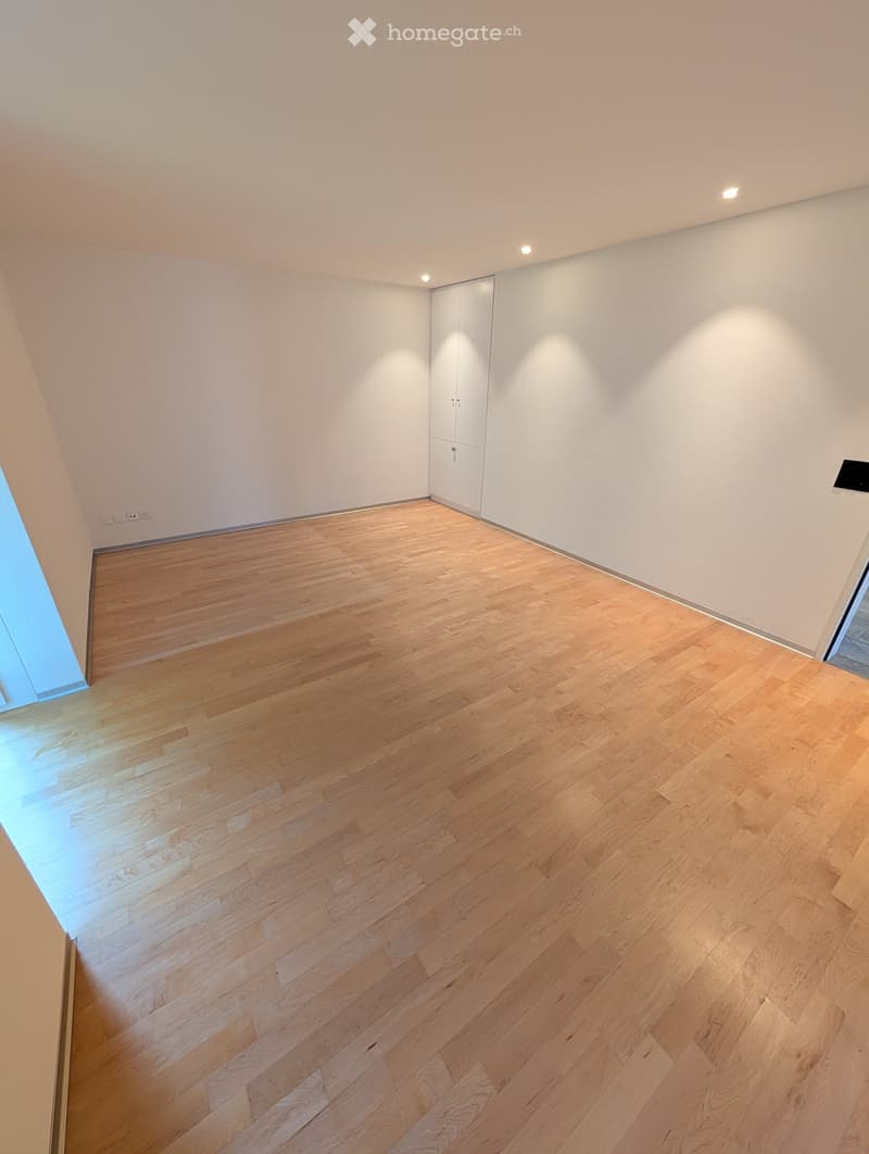 Empty room with light wooden flooring and white walls, featuring built-in closet doors and recessed lighting.