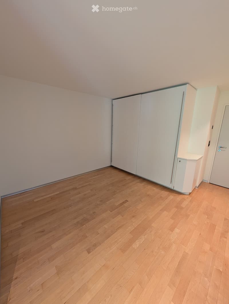 Empty room with light wooden flooring and white walls, featuring built-in white closet units and a closed door.