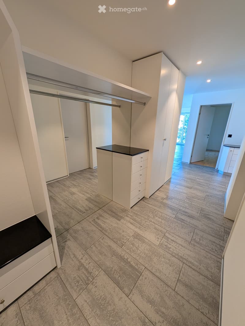 Empty hallway with tiled floor, white walls, built-in closet with sliding doors, and a small bench with a black top.
