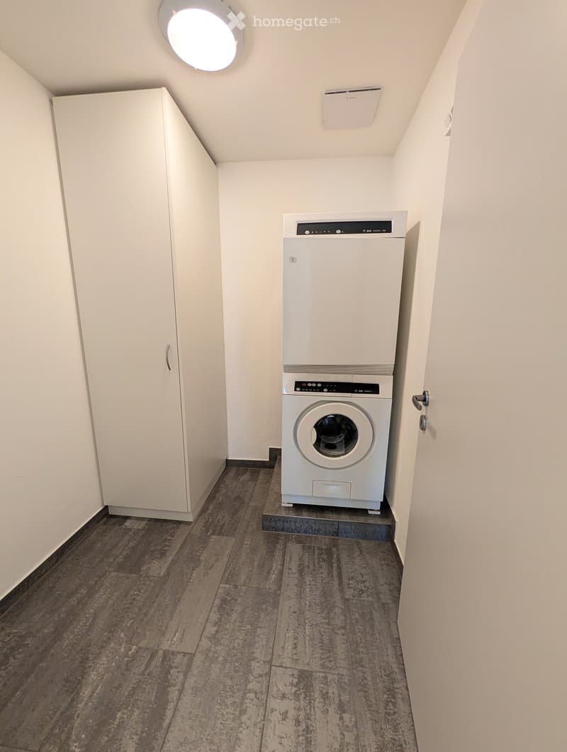 Narrow hallway with a private washing machine and dryer unit, white walls, and a round ceiling light.