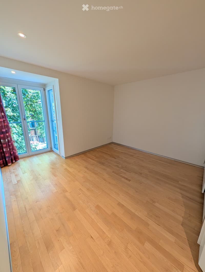 Empty room with light wooden flooring, white walls, and large sliding glass doors leading to a balcony.