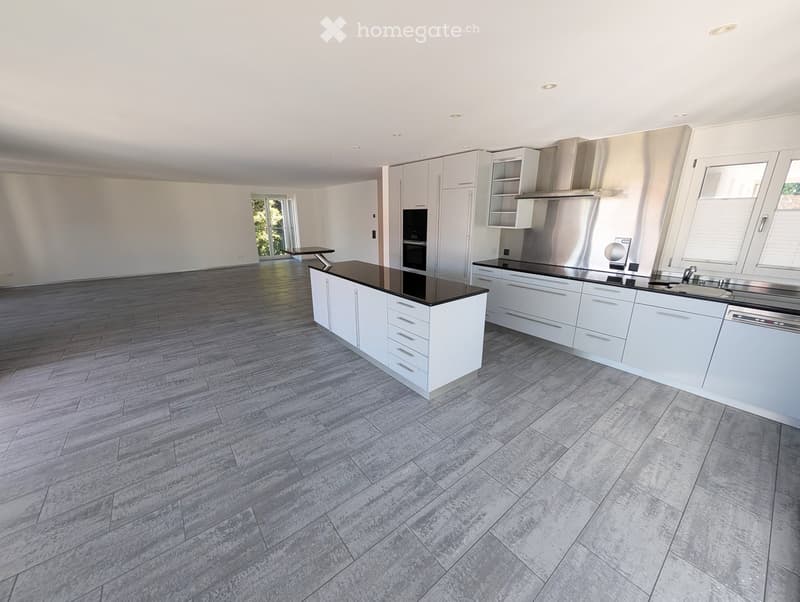 Modern, fully equipped kitchen with white cabinets, a central island, stainless steel appliances, and large windows.
