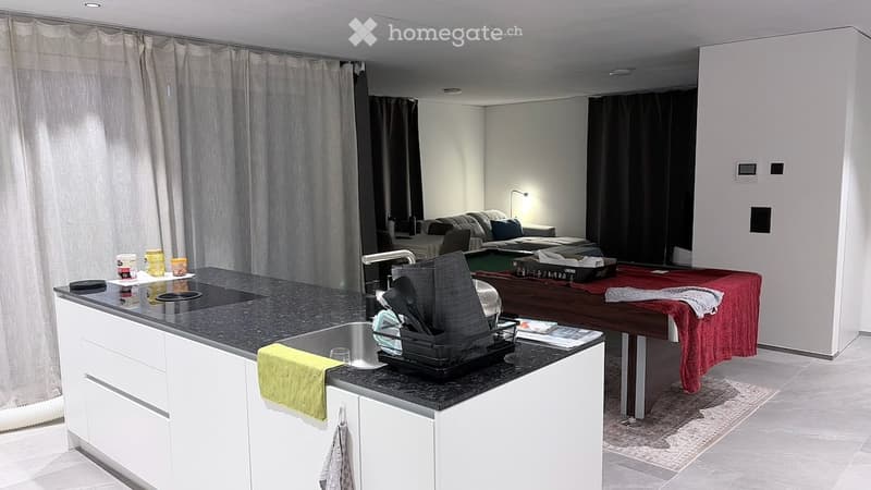 A modern, open-plan kitchen and living area with white cabinets, a black countertop, a sink, a sofa, and a dining table with chairs.