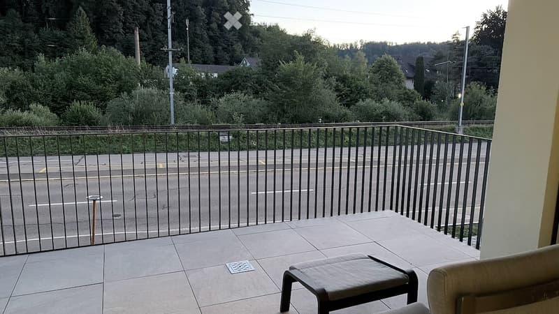 Balcony with tiled floor, metal railing, and outdoor furniture including a chair and small table.