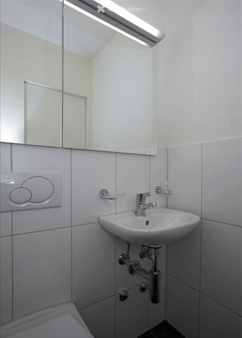 Modern bathroom with white tiles, a single sink, a large mirror, and a toilet.