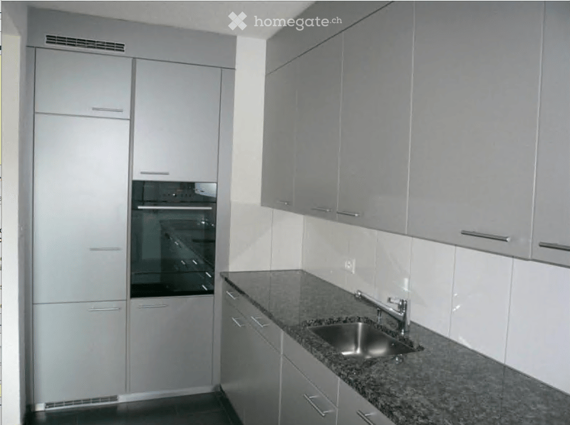 Modern kitchen with grey cabinets, granite countertop, stainless steel sink, and built-in oven.