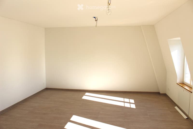 Empty room with wooden flooring and white walls, featuring a small window with a wooden sill and a light fixture on the ceiling.