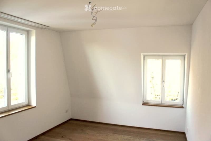 Completely empty room with wooden flooring, white walls, and two windows, one with a wooden sill.