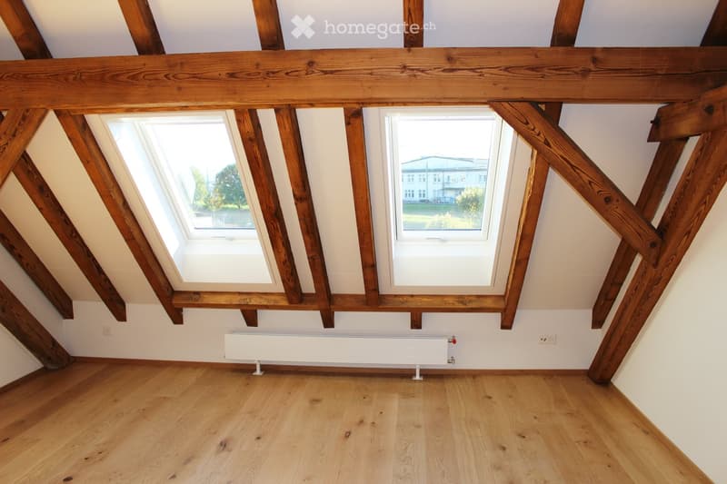 Empty attic room with wooden beams, skylights, and wooden flooring.