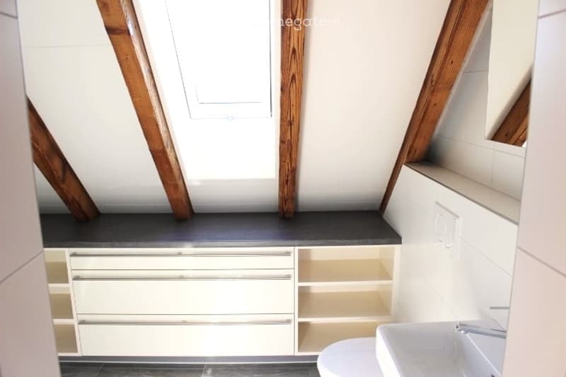 Modern bathroom with white tiled walls, dark grey countertop, white cabinetry, and exposed wooden beams on the ceiling.