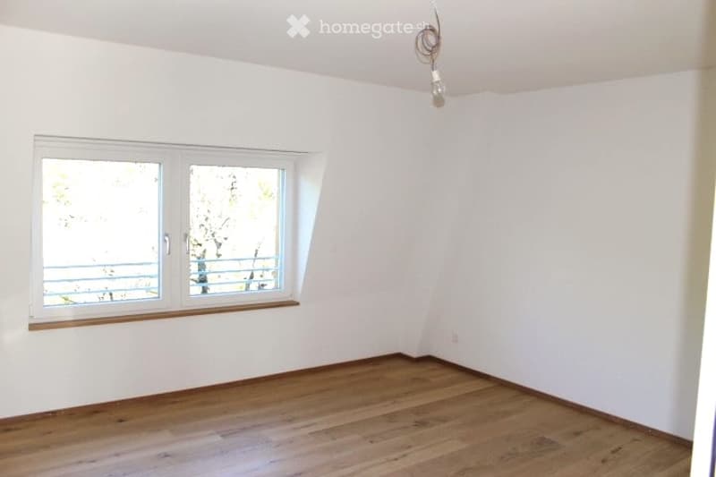 Empty room with white walls, wooden floor, and a large window with a view of a balcony.