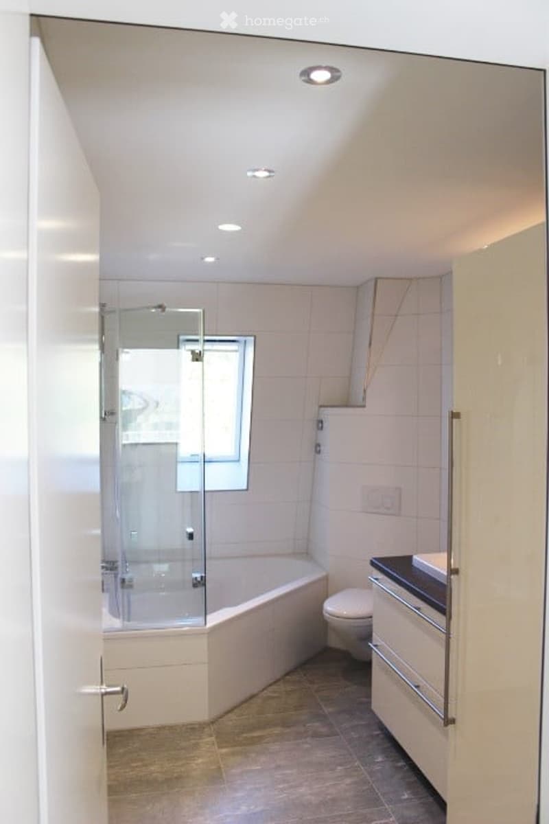 Modern bathroom with a white tiled shower stall, bathtub, toilet, sink, and built-in cabinetry. The space features recessed lighting and a window above the bathtub.
