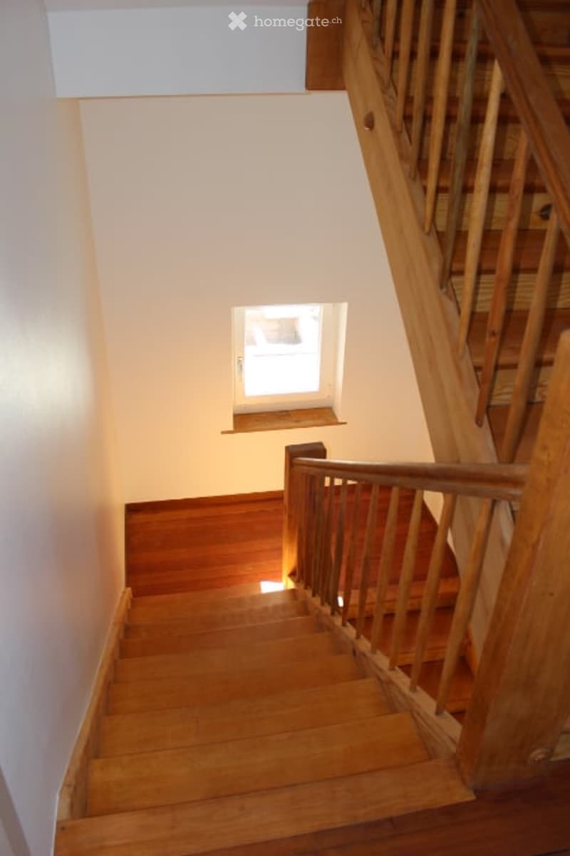 Wooden staircase with a handrail and a small window at the top, leading to an upper level.