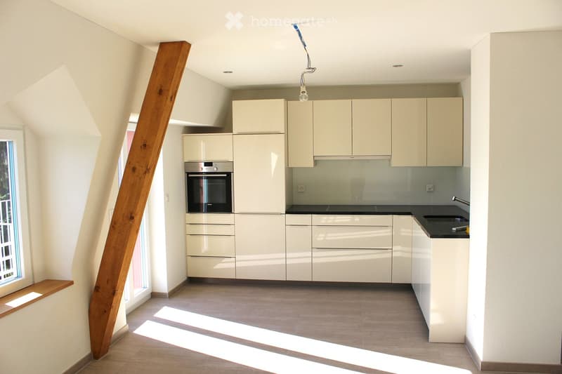 Modern kitchen with light-colored cabinets, stainless steel oven, black countertop, and a window letting in natural light.