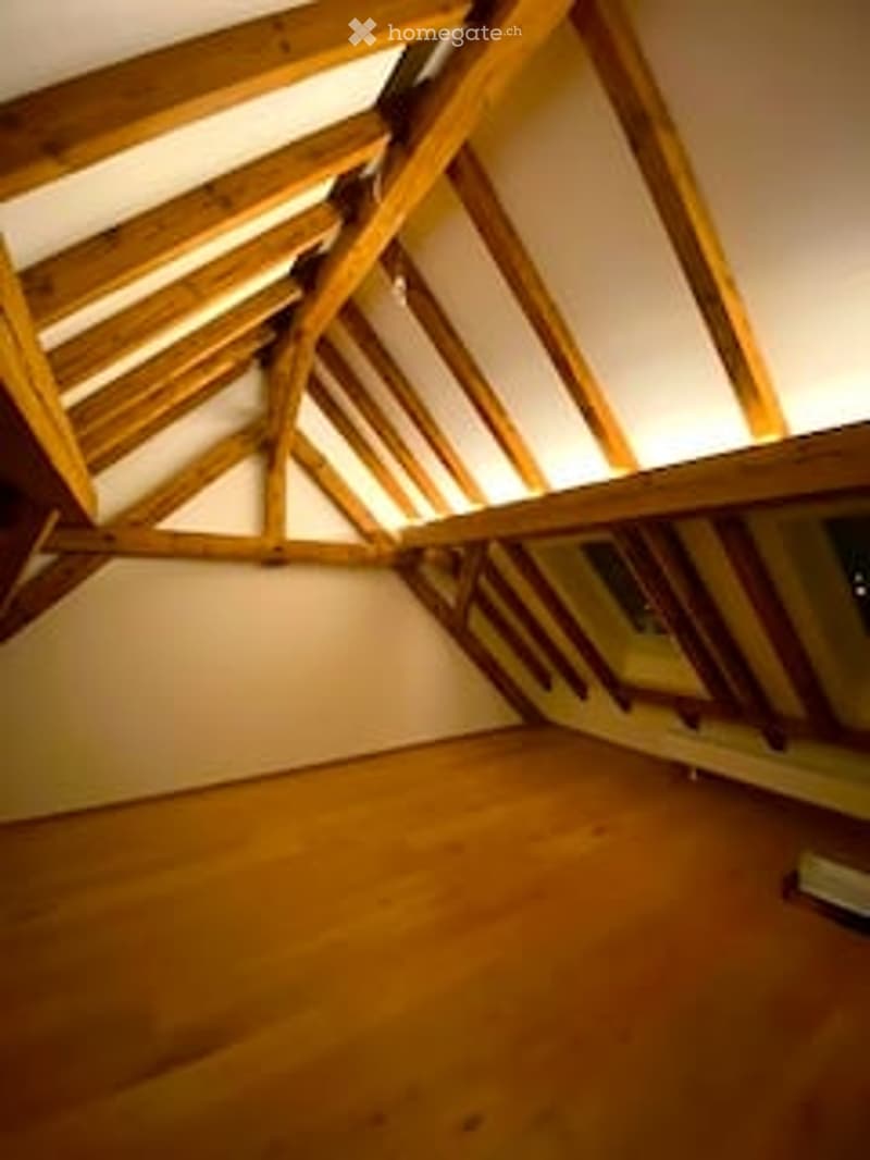 An attic space with exposed wooden beams and skylights, featuring a wooden floor and white walls.