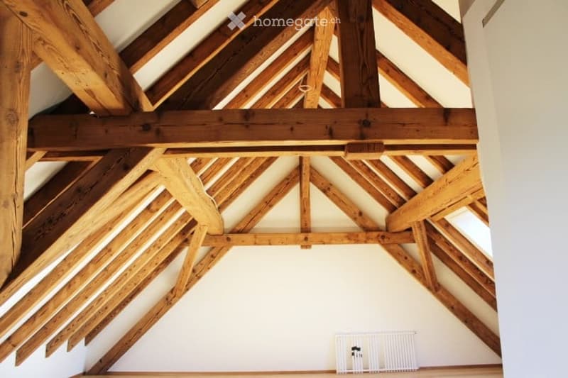 An attic space with exposed wooden beams and a white radiator on the wall. The room is completely unfurnished, showing only the structural elements and basic fixtures.