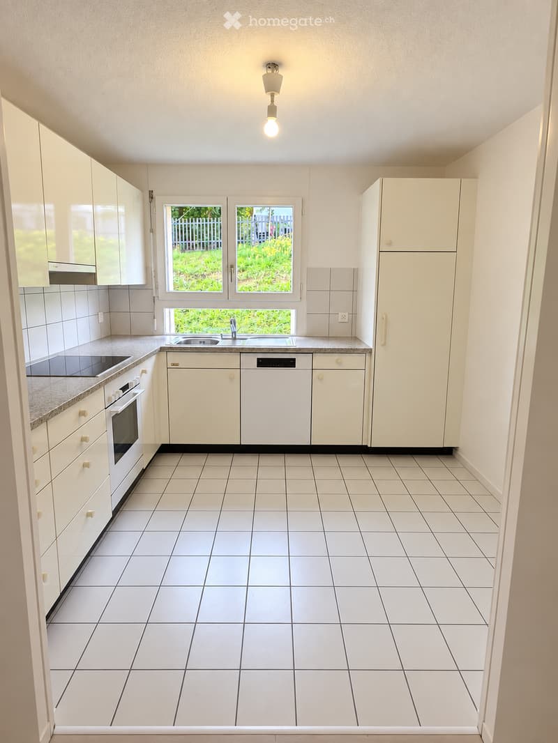 Modern kitchen with white cabinets, tiled floor, and stainless steel appliances including a refrigerator, oven, and dishwasher. Features a central island with a sink and ample natural light from windows.