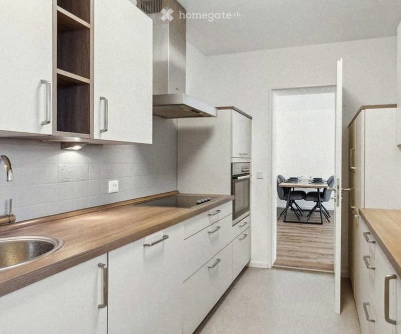 Modern kitchen with white cabinets, wooden countertops, stainless steel sink, and a small dining area with a table and chairs.