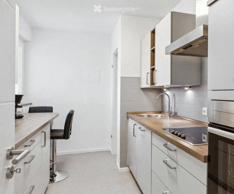 Modern kitchen with white cabinets, wooden countertops, stainless steel appliances, and a bar stool.