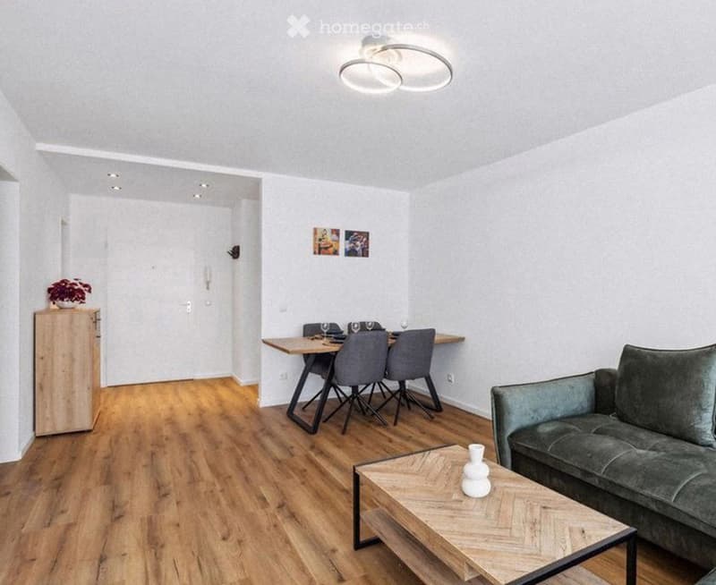 Modern living and dining area with wooden flooring, grey sofa, coffee table, dining table with chairs, and a small cabinet with a plant.
