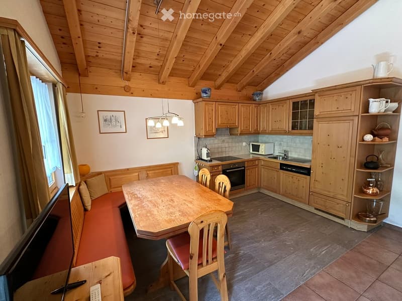 Cozy, wooden-furnished room with a sofa, dining table, chairs, kitchen area, and wooden cabinets.