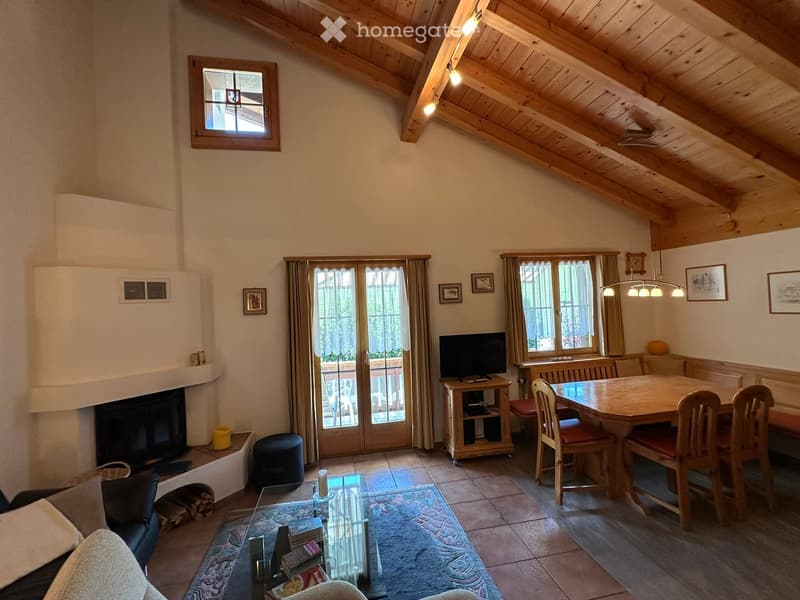 Cozy living and dining area with exposed wooden beams, fireplace, large windows, and balcony access.