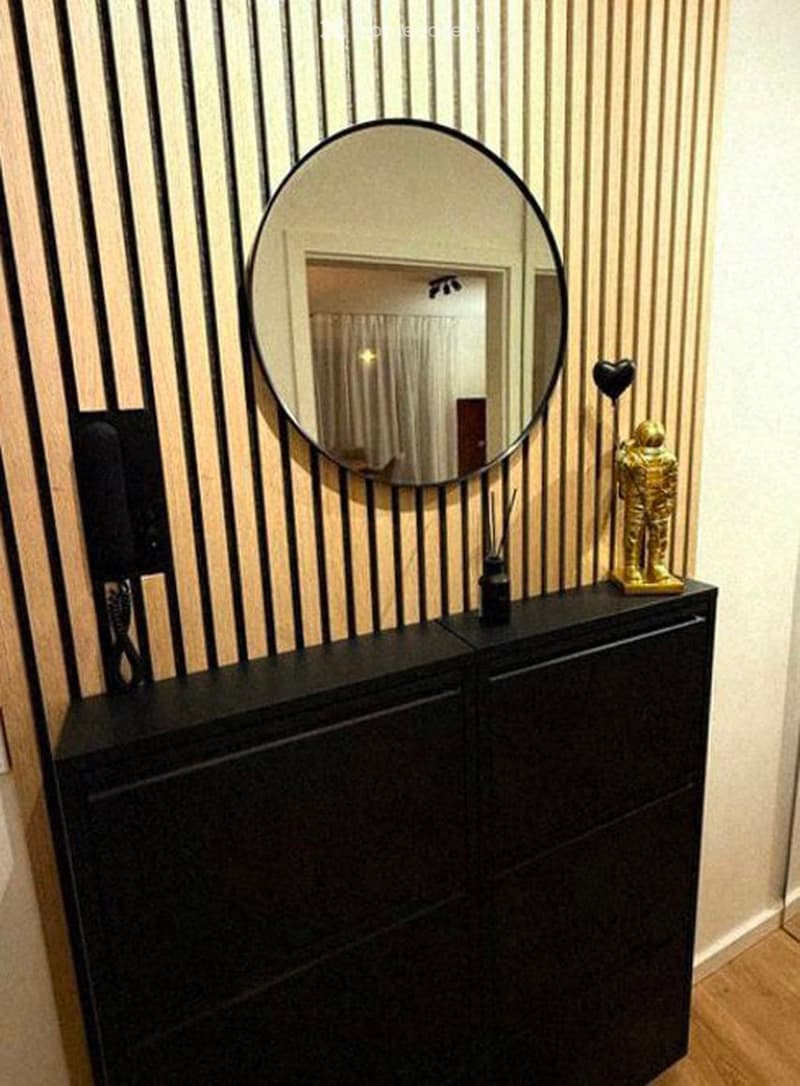 A stylish hallway or entryway with a large round mirror, a black cabinet, a golden statue, and a decorative vase.