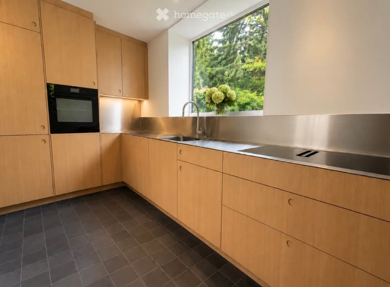 Modern kitchen with light wooden cabinets, stainless steel sink, and dark tiled floor.