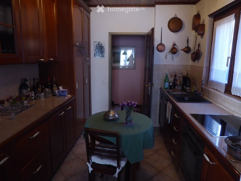 Wooden cabinets, tile floor, small dining table with green tablecloth, kitchen appliances, pots and pans on the wall