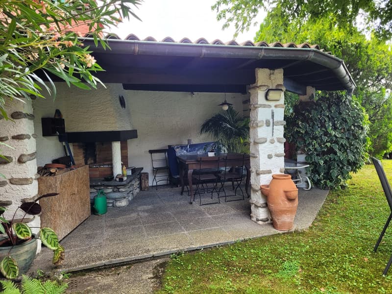 A covered outdoor patio with a stone fireplace, dining table and chairs, potted plants, and decorative vases.