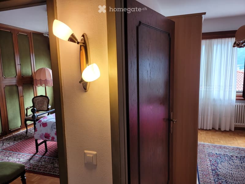 Bedroom with wooden furniture, floral chair, wall sconces, and a dark wooden door