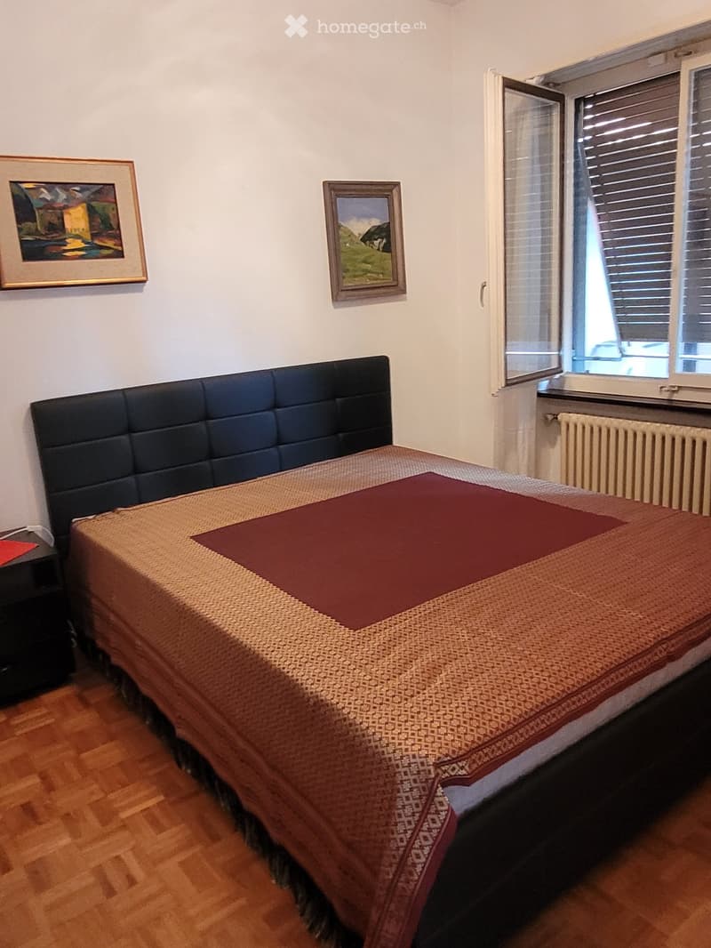 Bedroom with a large bed, black leather headboard, framed artwork on the walls, and a window with blinds.