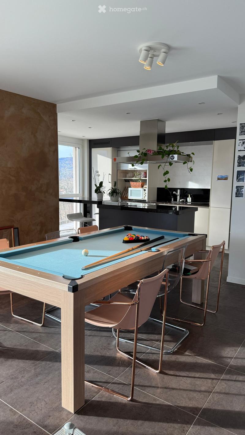 Modern kitchen with a pool table, bar stools, and a kitchen island. The space features contemporary design elements, including a sleek kitchen area with a microwave, potted plants, and a faucet.