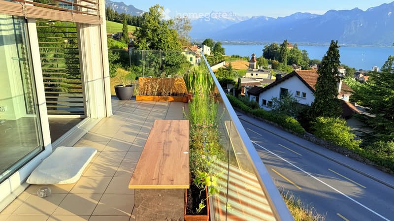 Balcony with wooden bench, potted plants, and scenic mountain and lake view.