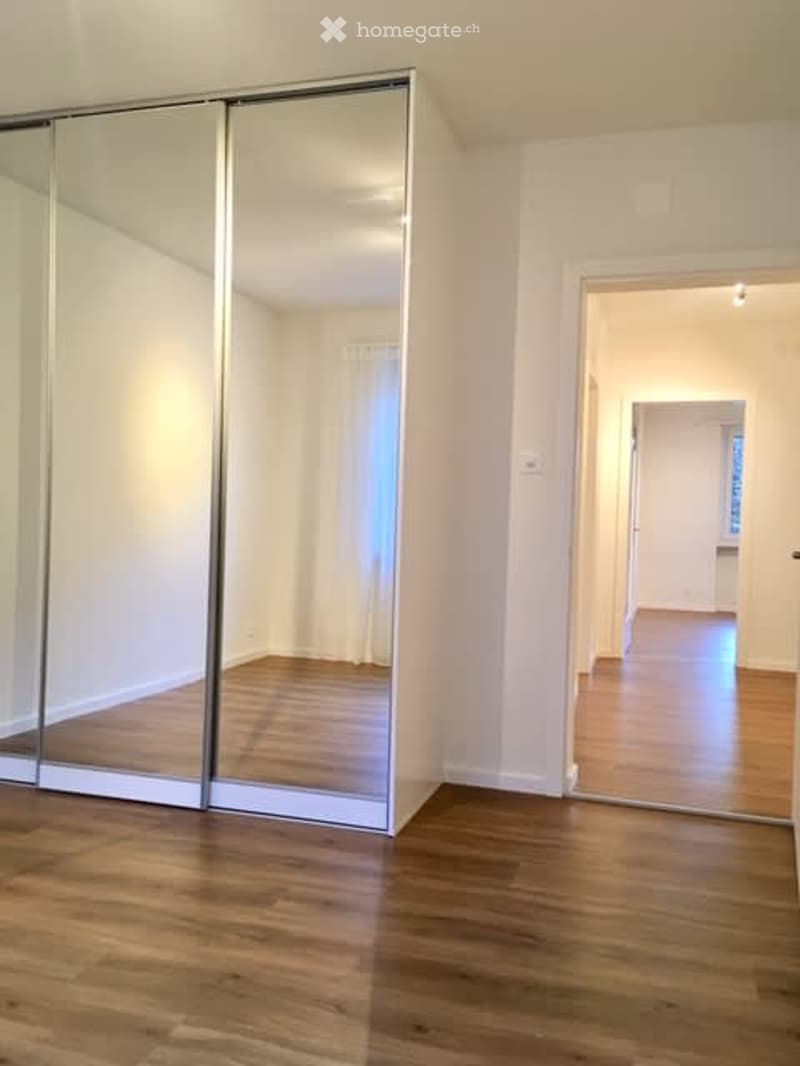 Empty room with wooden flooring, large mirrored closet, and an open doorway leading to another room.