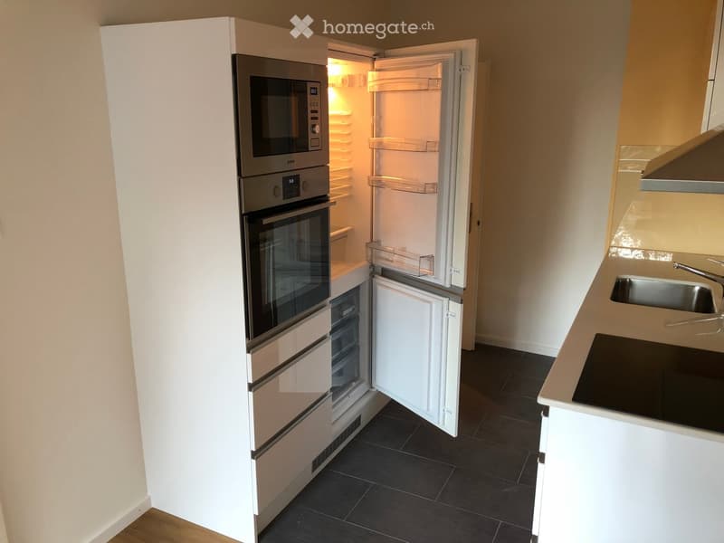 Modern kitchen with white cabinets, stainless steel appliances, and dark tiled flooring.