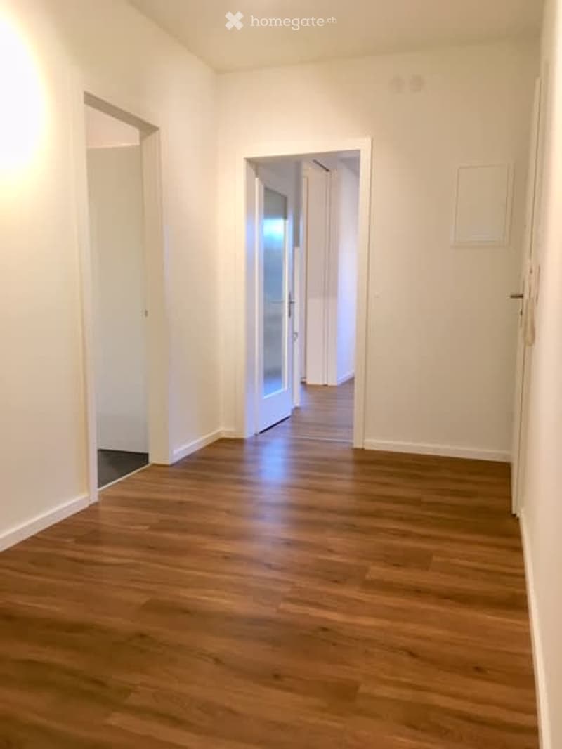 Empty room with wooden flooring and white walls, featuring multiple doorways leading to other spaces.