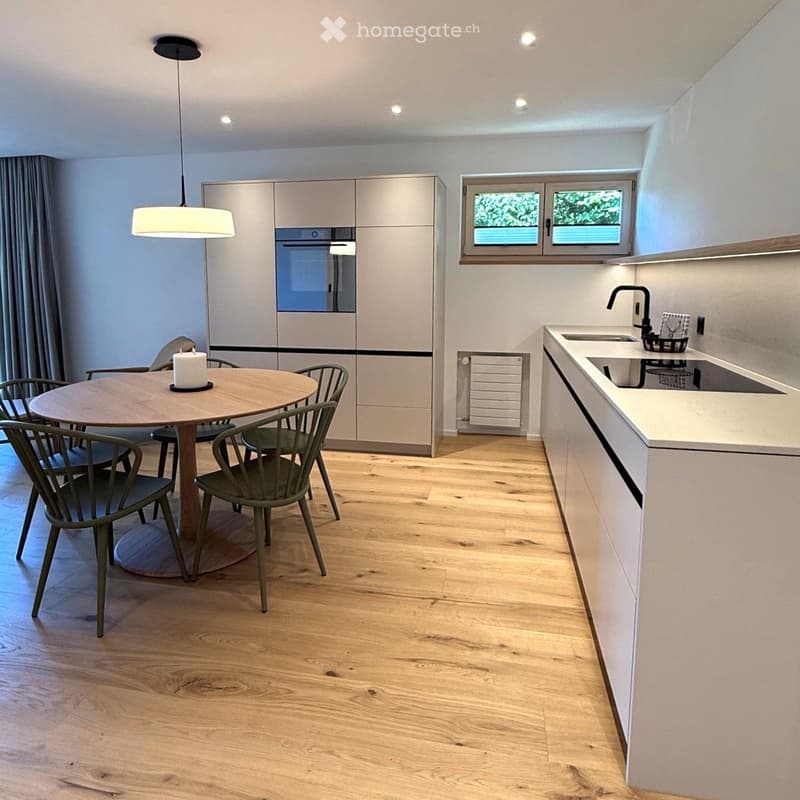 Modern kitchen with light-colored cabinets, a round dining table with six chairs, a sink with a modern faucet, and a pendant light hanging above the table.