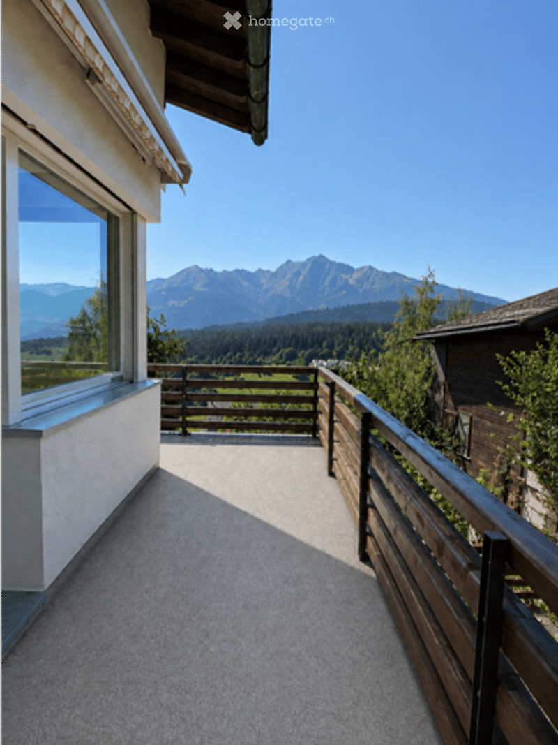 Balcony with wooden railing, overlooking a scenic mountain landscape and forested area.