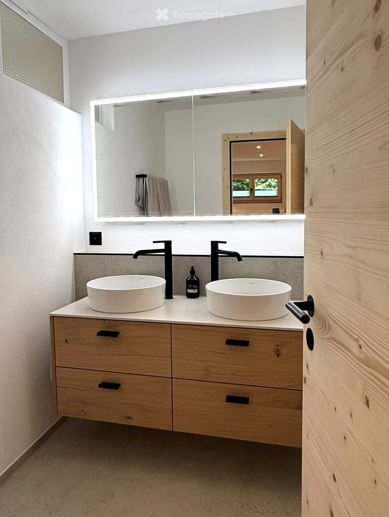 Modern bathroom with double sink vanity, wooden cabinet, sleek black faucets, large mirror, and a towel hanging on the side.
