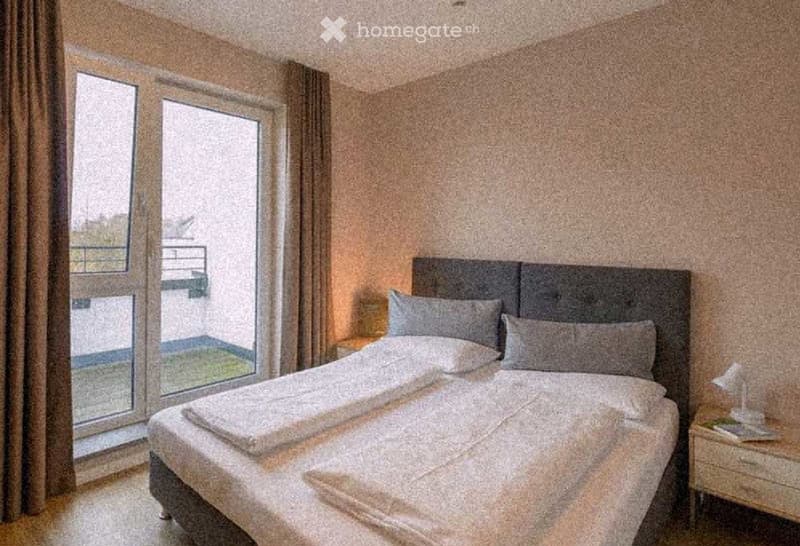 Modern bedroom with a large bed, headboard, pillows, and a nightstand near a large window with a view of a balcony area.