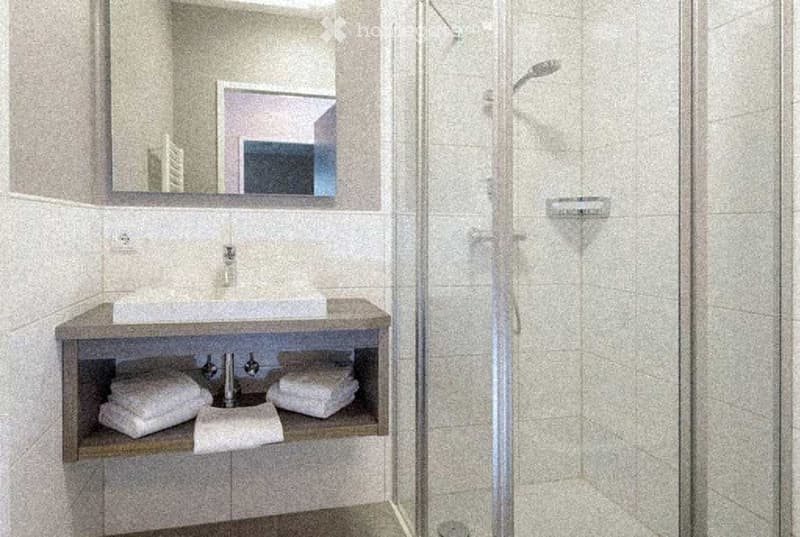 Modern bathroom with a sink, mirror, and a glass-enclosed shower area. The sink has a wooden shelf below holding neatly folded towels.