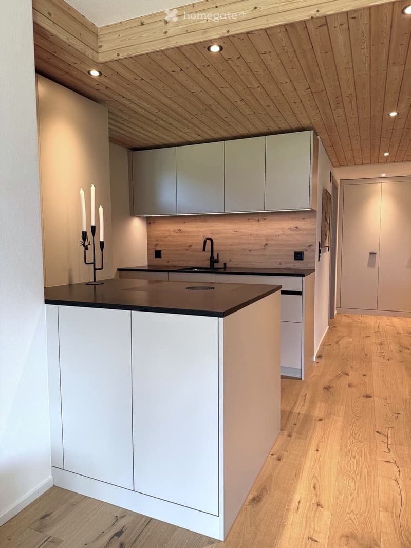 Modern kitchen with white cabinets, wooden ceiling, and a black countertop. Features a sink with a faucet and a candle holder on the counter.