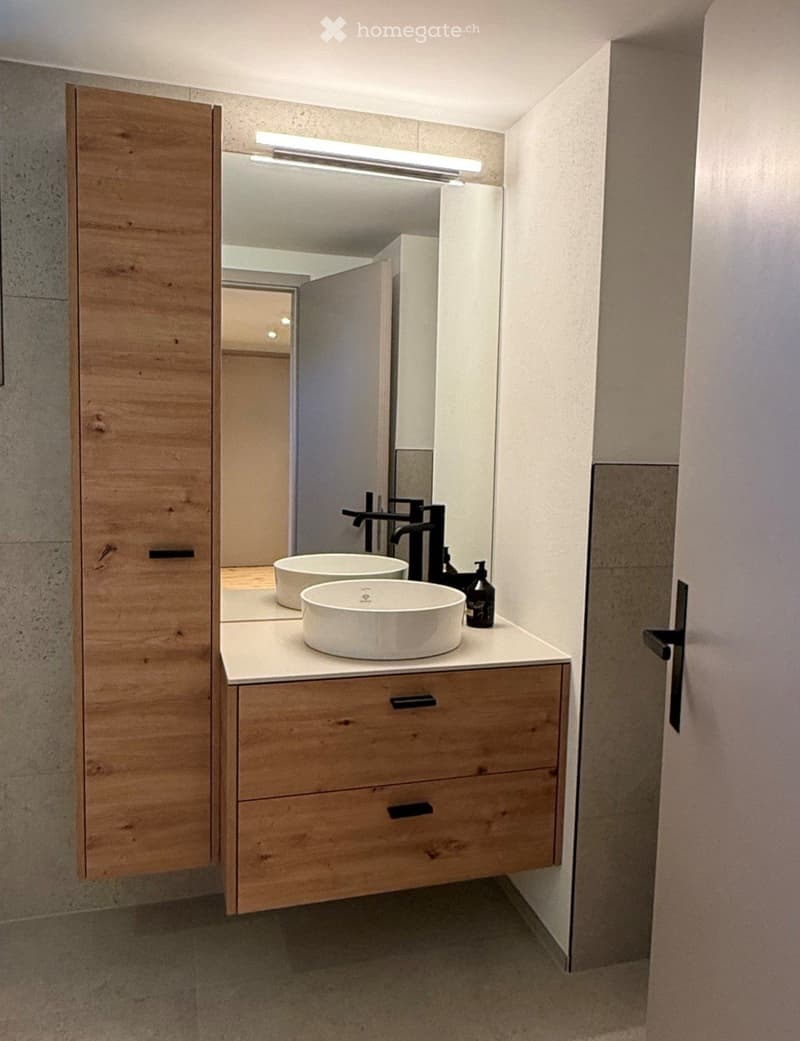 Modern bathroom with a wooden vanity, two round sinks, a large mirror, and a sleek faucet.