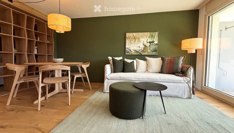 Modern living room with a white sofa, green cushions, a round coffee table, a dining area with a table and chairs, a bookshelf, and pendant and floor lamps.
