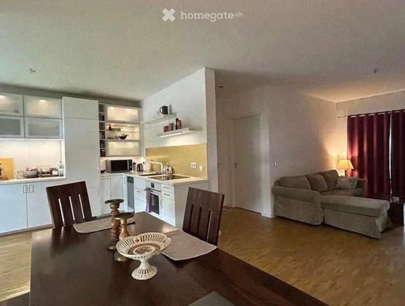 Open-plan living and dining area with a sofa, dining table, chairs, and a modern kitchen featuring white cabinets, a microwave, oven, and sink.