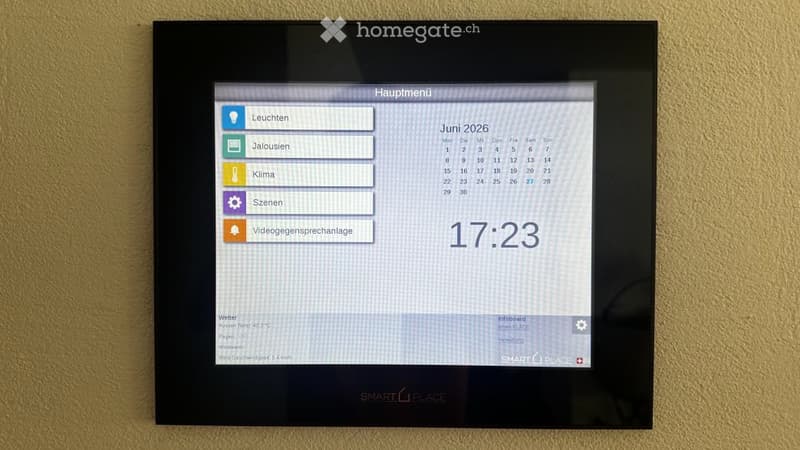 A wall-mounted smart home control panel displaying a menu with options for lights, alarms, climate, scenes, and video call scheduling, along with a digital clock and weather information.