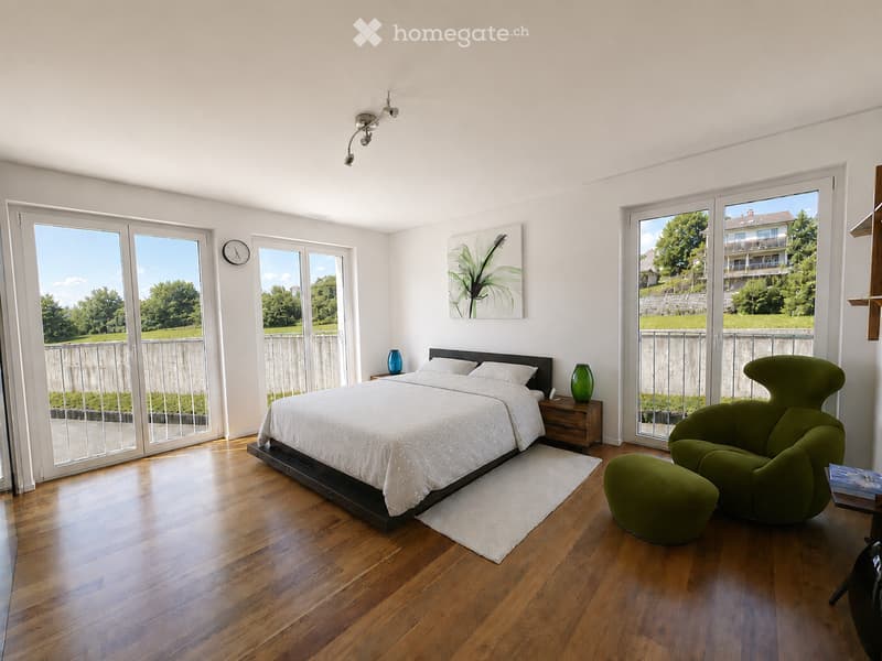 Bright bedroom with wooden flooring, large windows, a double bed with white bedding, a nightstand with a blue vase, a green armchair with a matching stool, and a painting on the wall.