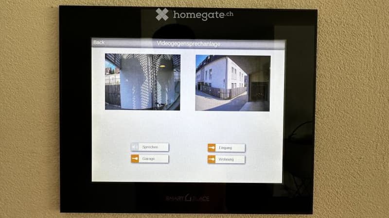 A wall-mounted interactive screen displaying options for video communication, showing images of a building and a garage.