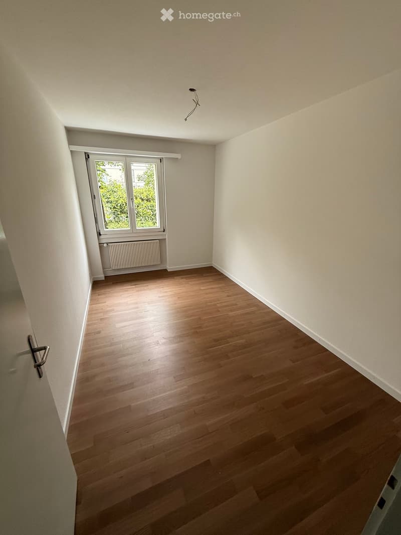 Empty room with wooden flooring, white walls, and a window with a radiator below it.